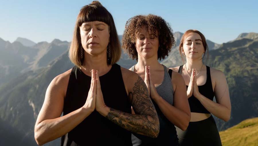 Yogafrühling Gastein. Drei Frauen machen Yoga auf einem Berggipfel, umgeben von den Alpen und der strahlenden Sonne. #Yoga #Berge #Entspannung