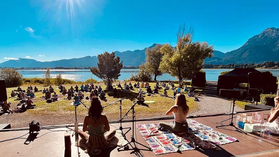 Om am See Yogafestival. Yoga am See, im Hintergrund Berge, sonnig