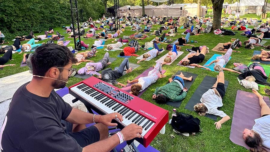Yoga Beach Festivals von NamastÃ United, Ein Mann spielt ein rotes Keyboard auf einer Wiese, vor ihm wird Yoga gemacht